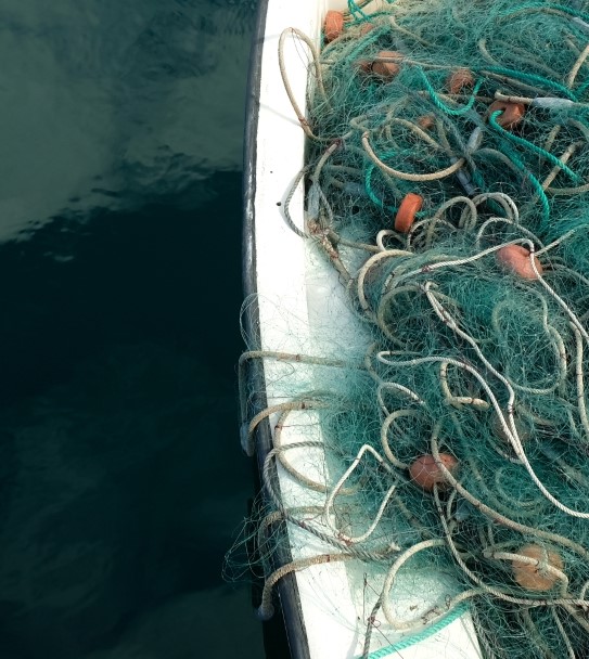 Fishing net in a small fishing boat. Horizontal panoramic crop with large area of dark blue water.