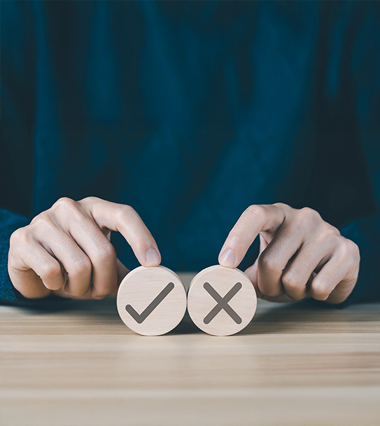 Hands hold wooden discs with a checkmark and an X, suggesting a choice.