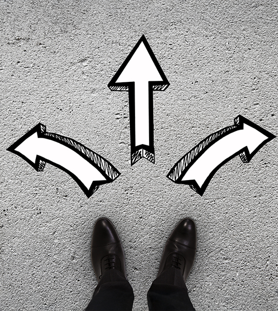 A person's feet stand at a crossroads with three arrows pointing in different directions on a textured gray surface.